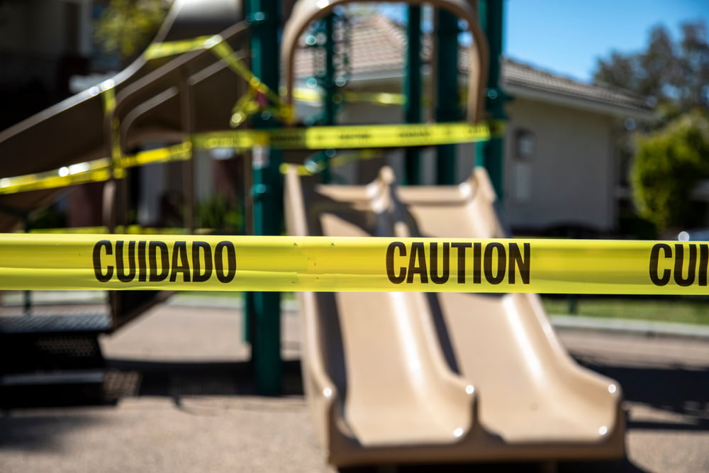 yellow caution tape in english and spanish barring access to playgound equipment at a park